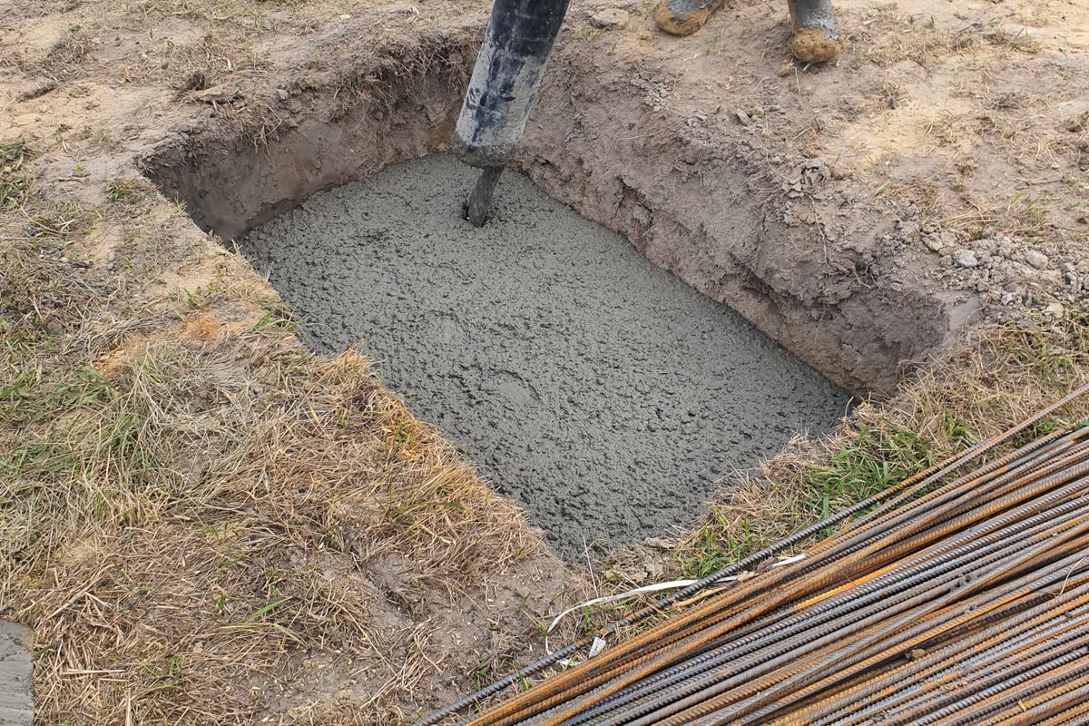 Wet concrete being poured into a footing trench beside steel reinforcing bar